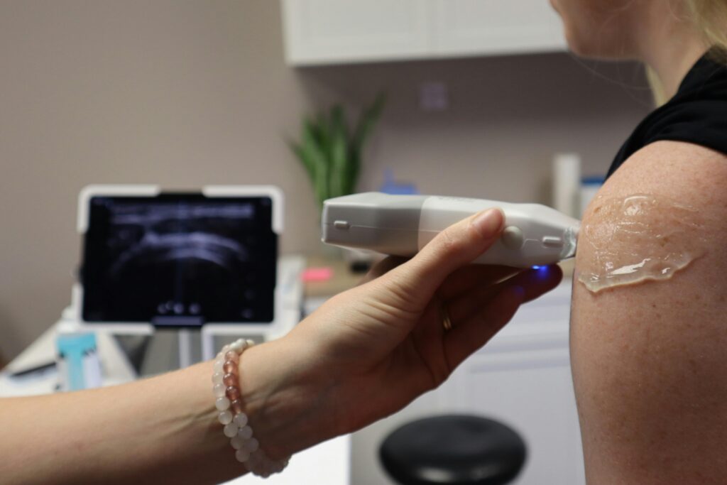 Doctor performing a shoulder ultrasound in a medical office with modern equipment.
